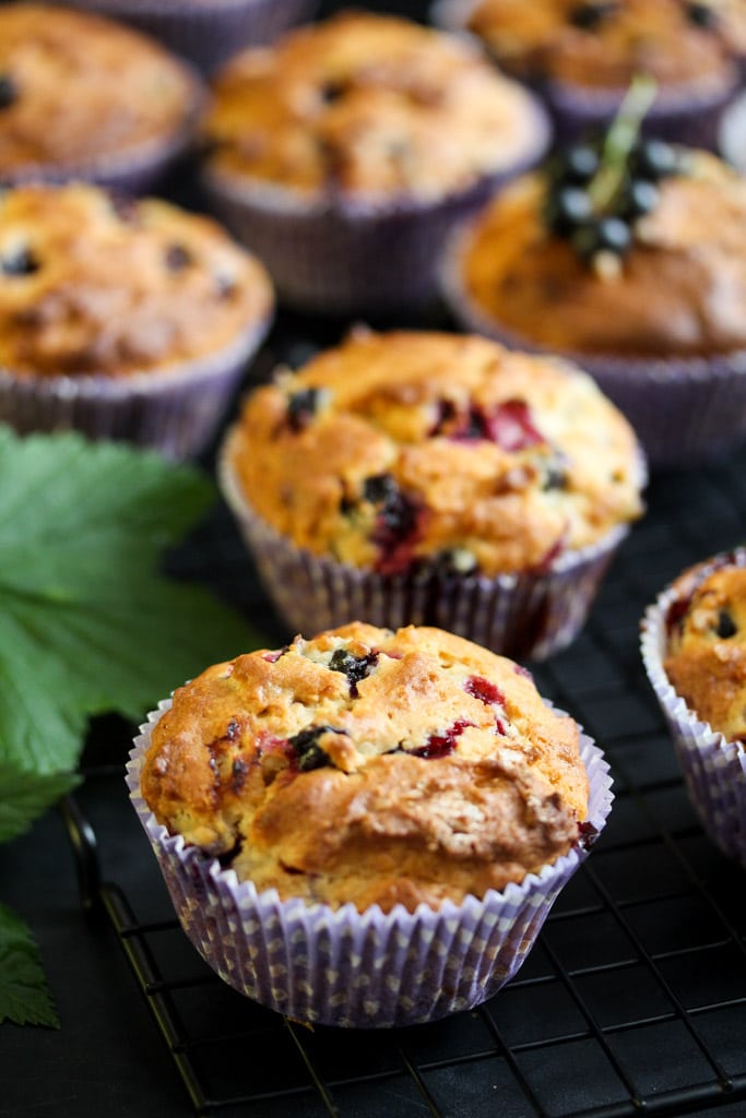 many berry cupcakes on a black table with leaves beside.