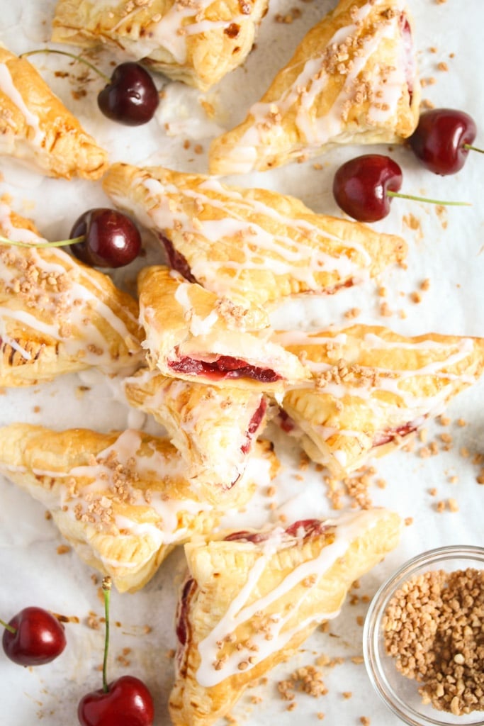 many turnovers piled on a the table and fresh cherries behind.