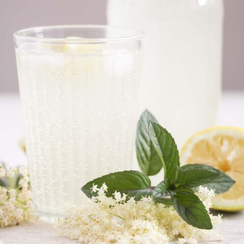 glass and bottle with non-alcoholic elderflower champagne on a white wooden board.