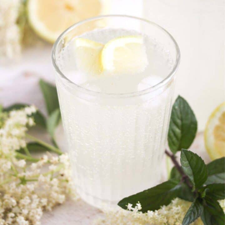 elderflower champagne in a glass with lemon slices and flowers around it.