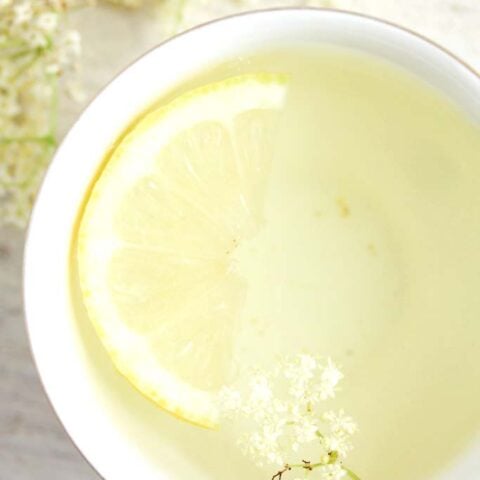 close up of clear yellow tea with half a lemon slice and petals inside.