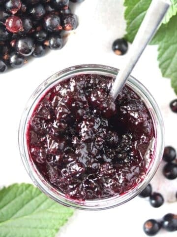 black currant jam and berries in a bowl with leaves around.