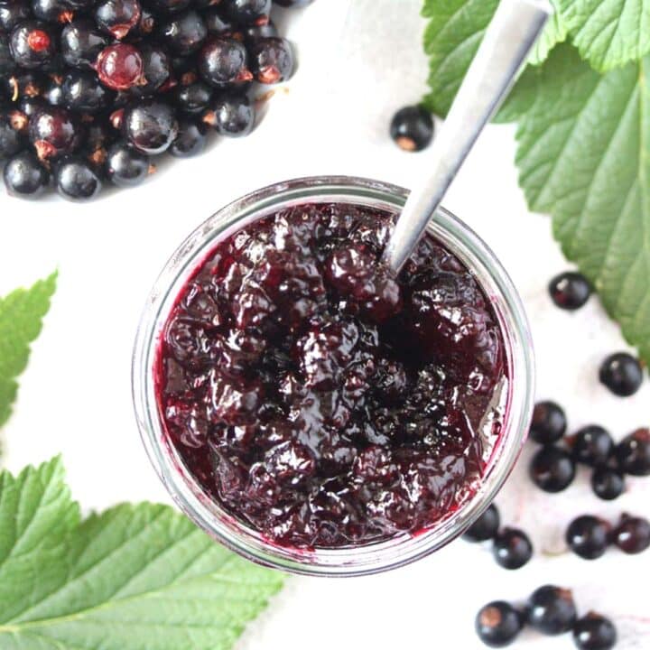 black currant jam and berries in a bowl with leaves around.