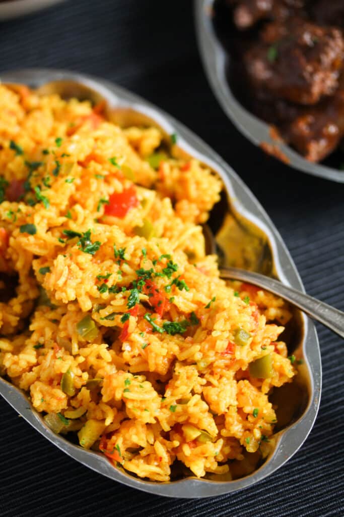 silver platter full of orange-colored rice with a spoon in it.