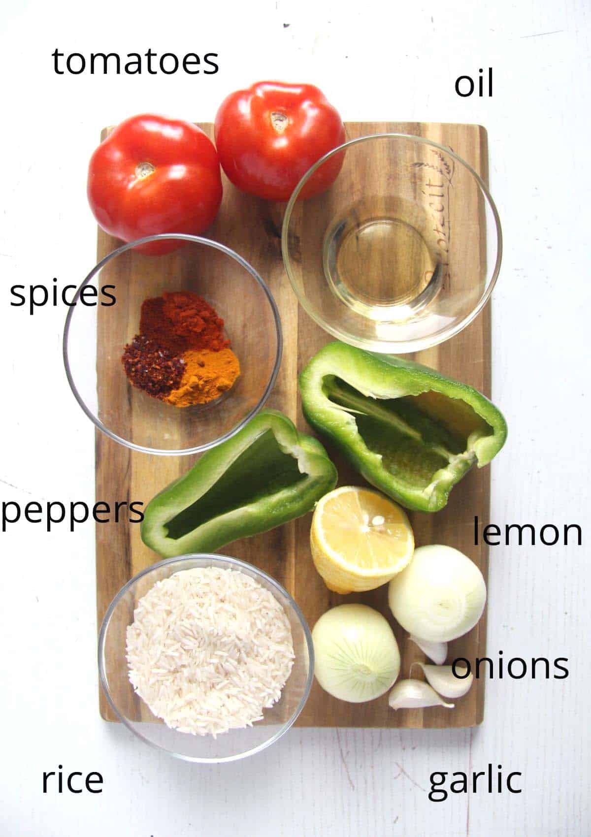 tomatoes, peppers, spices, oil, lemon, rice, garlic, onion on a wooden board.