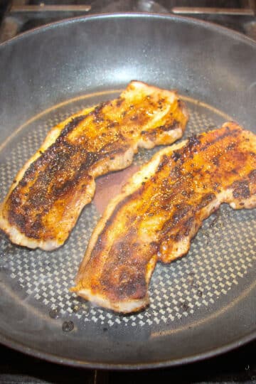 two pork belly slices in a nonstick frying pan.