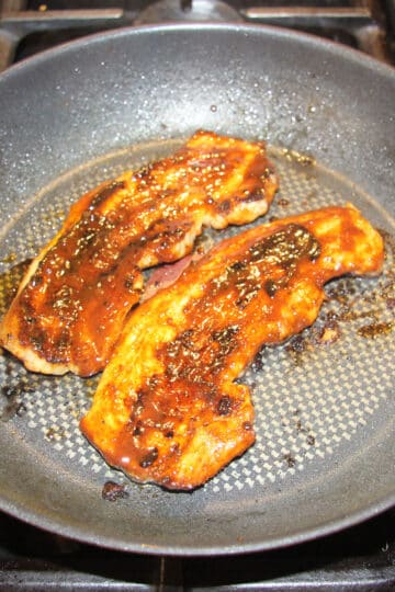 two long strips of pork belly cooking in a pan.