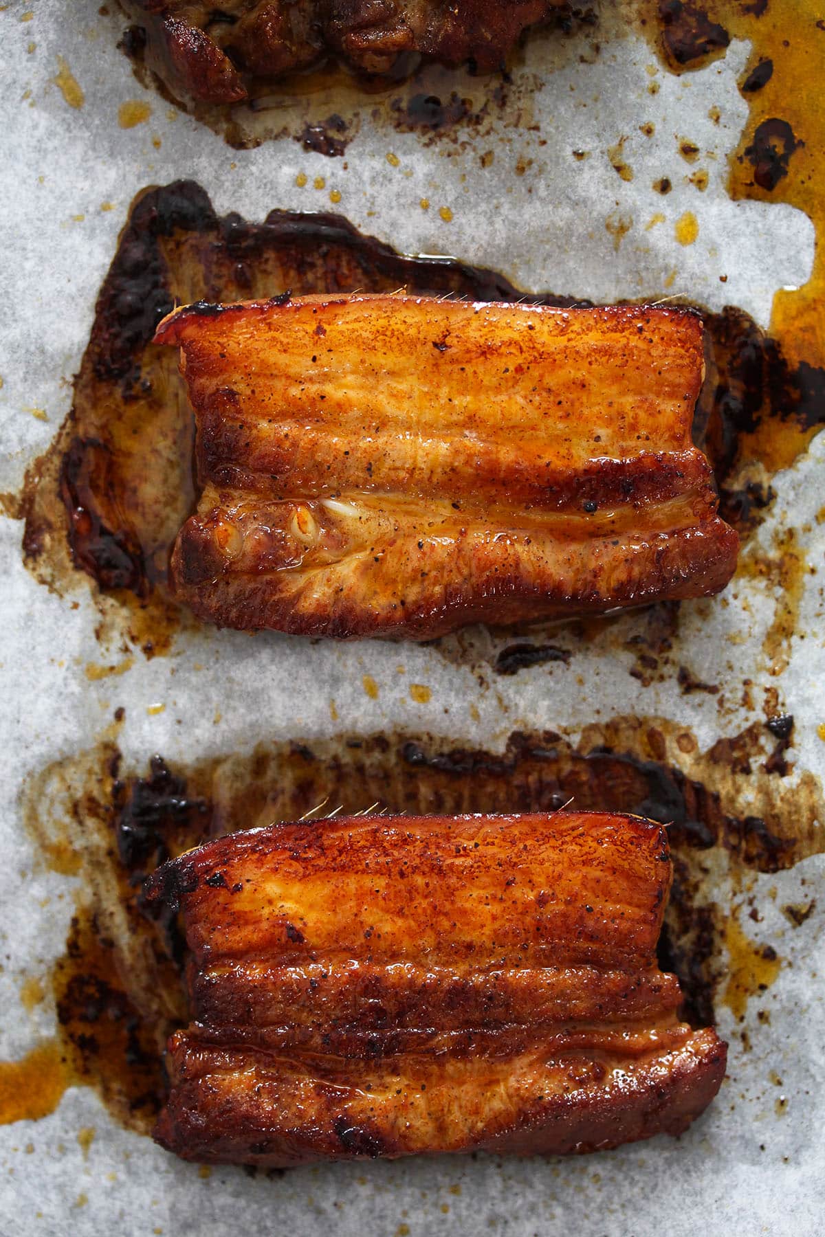 two pork belly strips on a baking sheet lined with parchment paper.