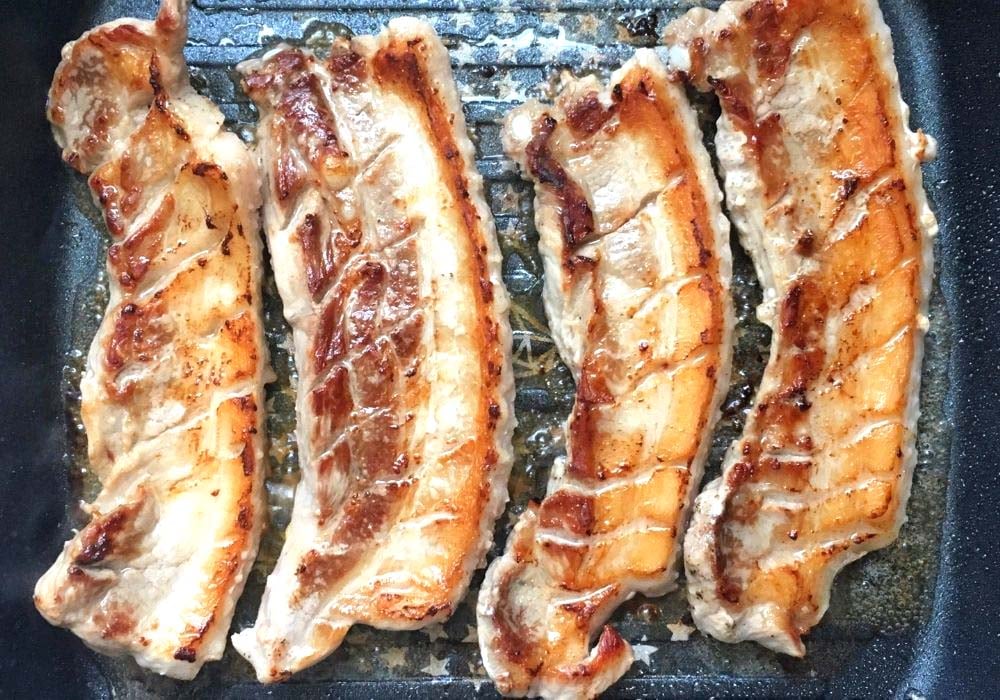 long belly strips being cooked in a grill pan.