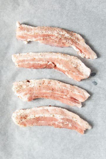 uncooked pork belly strips on parchment paper.