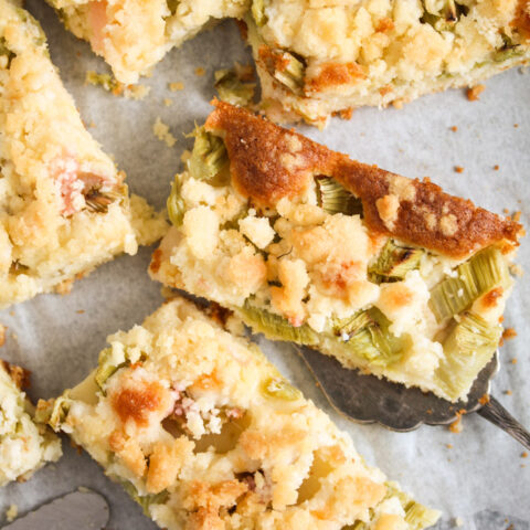 overhead view of several rhubarb crumble cake pieces on a baking tray lined with baking paper.