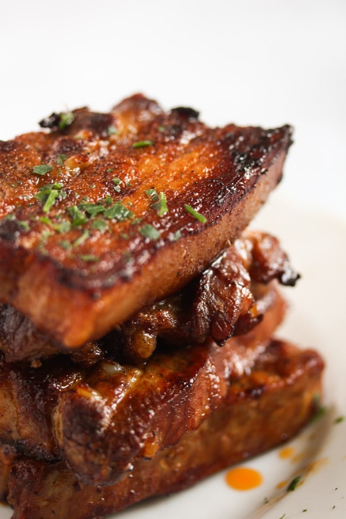 close up of a staple of pork belly strips sprinkled with parsley.