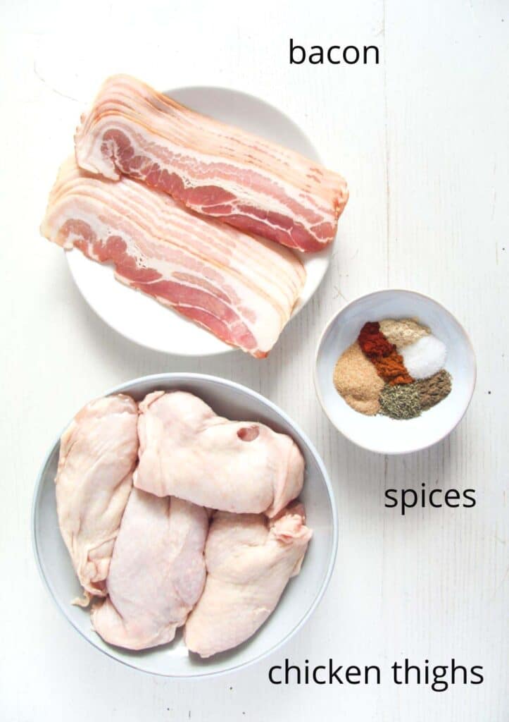raw bacon and chicken parts on plates, spices in a small bowl.
