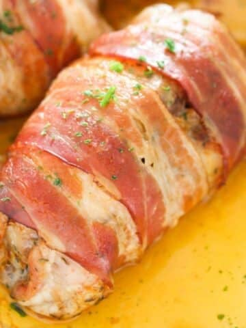 bacon wrapped chicken thighs close up in a pool of cooking juices.