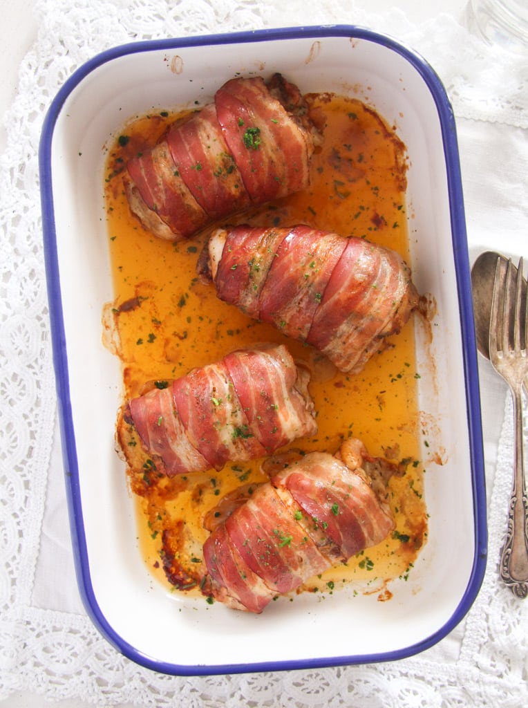 four rolls of meat with bacon in an enamel roasting dish.