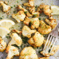 baked cauliflower on a tray with a fork and lemon slices.