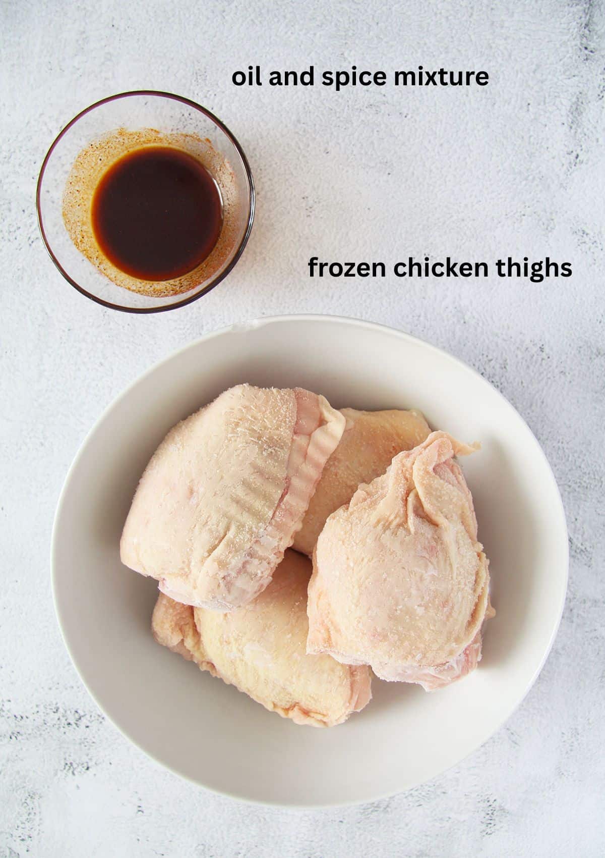 one bowl of oil and spice mixture and frozen chicken thighs in another bowl.