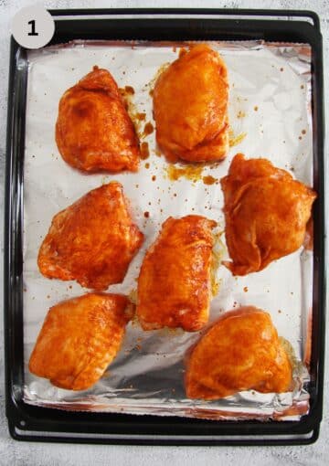frozen and seasoned chicken thighs on a baking sheet lined with foil.