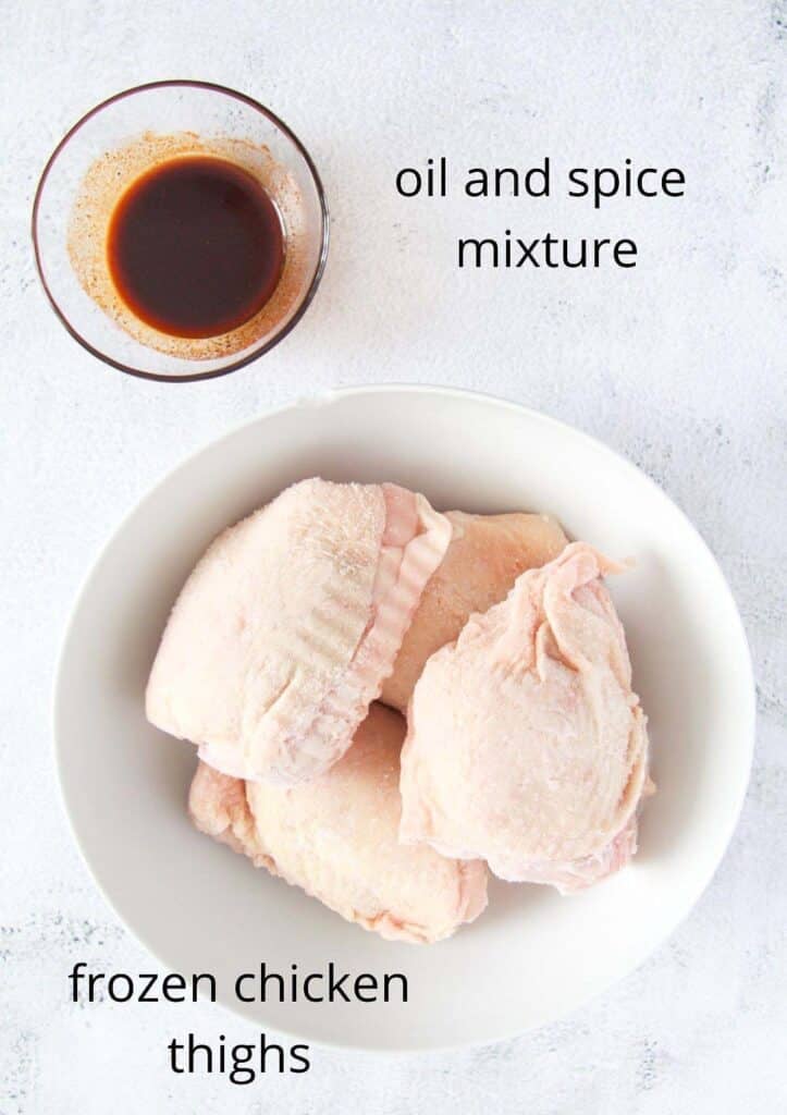 raw frozen chicken and a small bowl of spices mixed with oil.