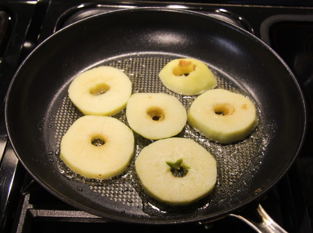 cored apple rings cooking in a cast-iron skillet.