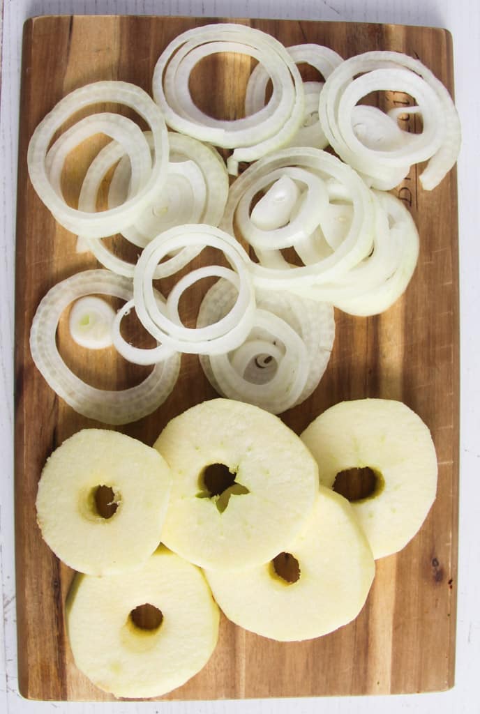 wooden board with sliced raw onions and apple rings.