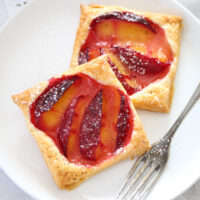 two pastry tartlets with fruit on a white plate with a vintage fork.