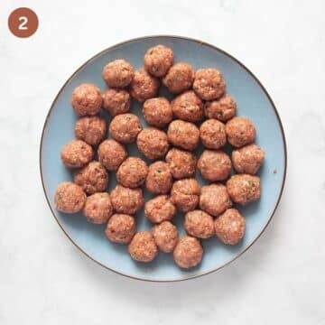 many little uncooked meatballs on a large blue plate.
