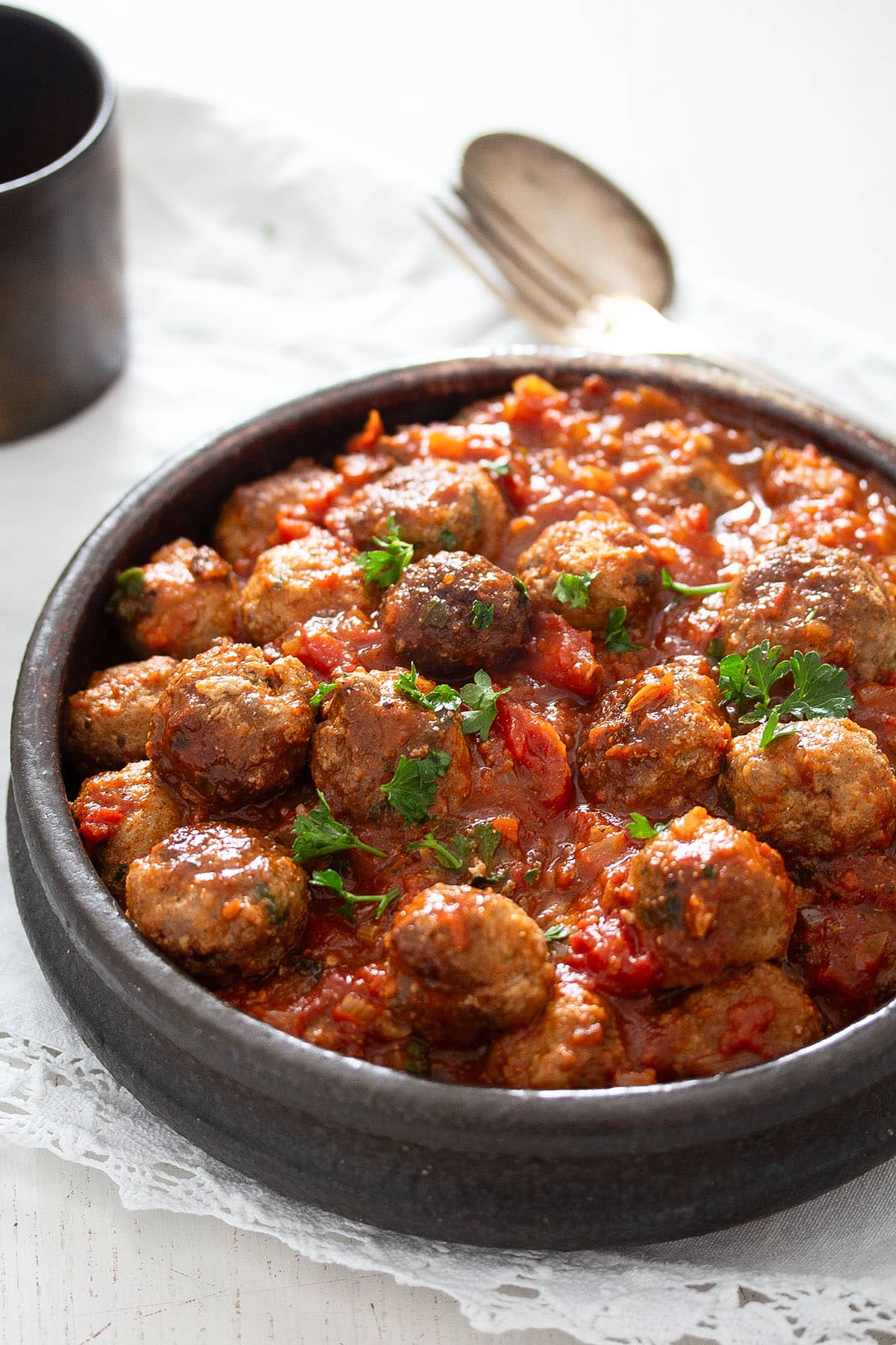 spanish meatballs or albondigas sprinkled with parsley in a small bowl. a spoon behind it. 