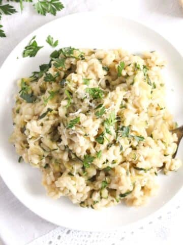 overhead view of a white plate with zucchini risotto sprinkled with parsley.