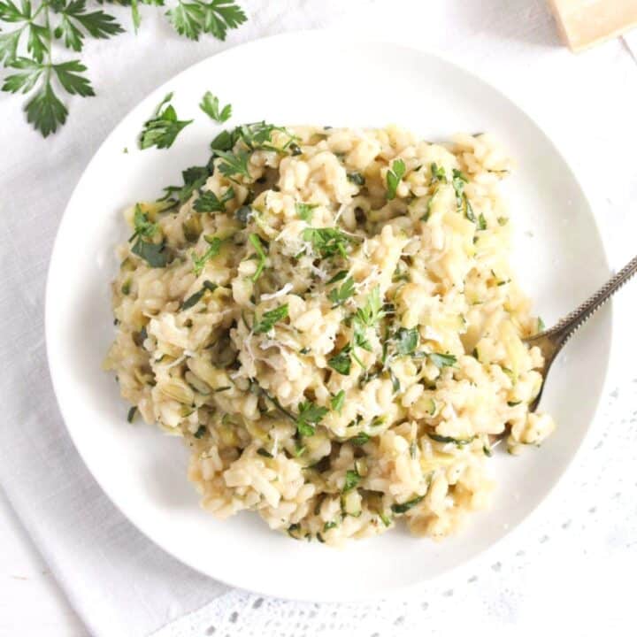 overhead view of a white plate with zucchini risotto sprinkled with parsley.