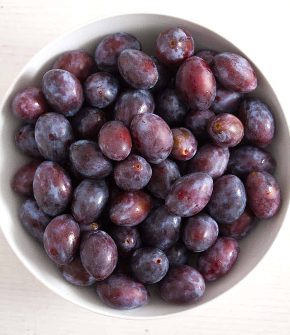 whole plums in a white bowl.