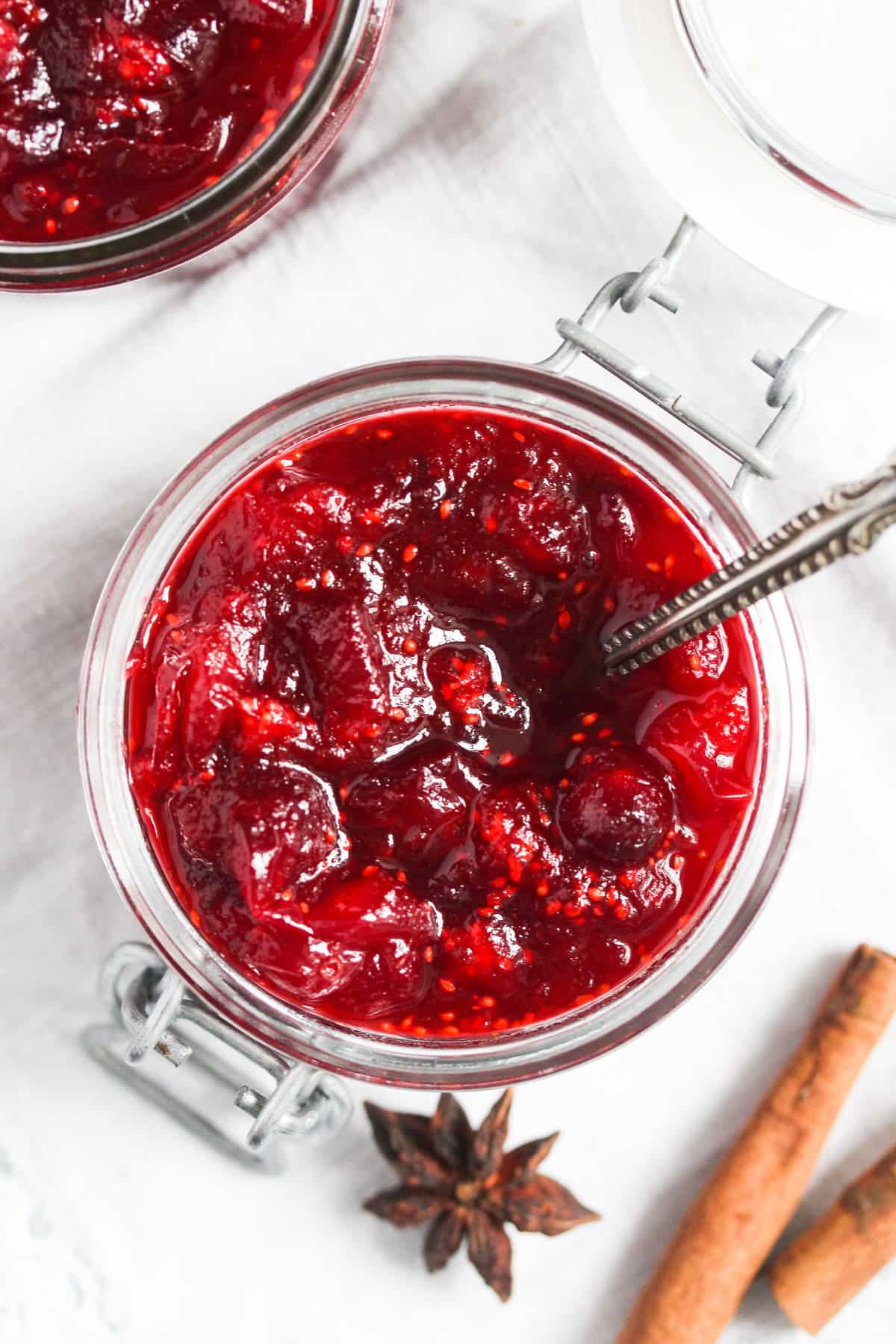 overhead view of cranberry sauce in a jar with star anise and cinnamon sticks beside it.
