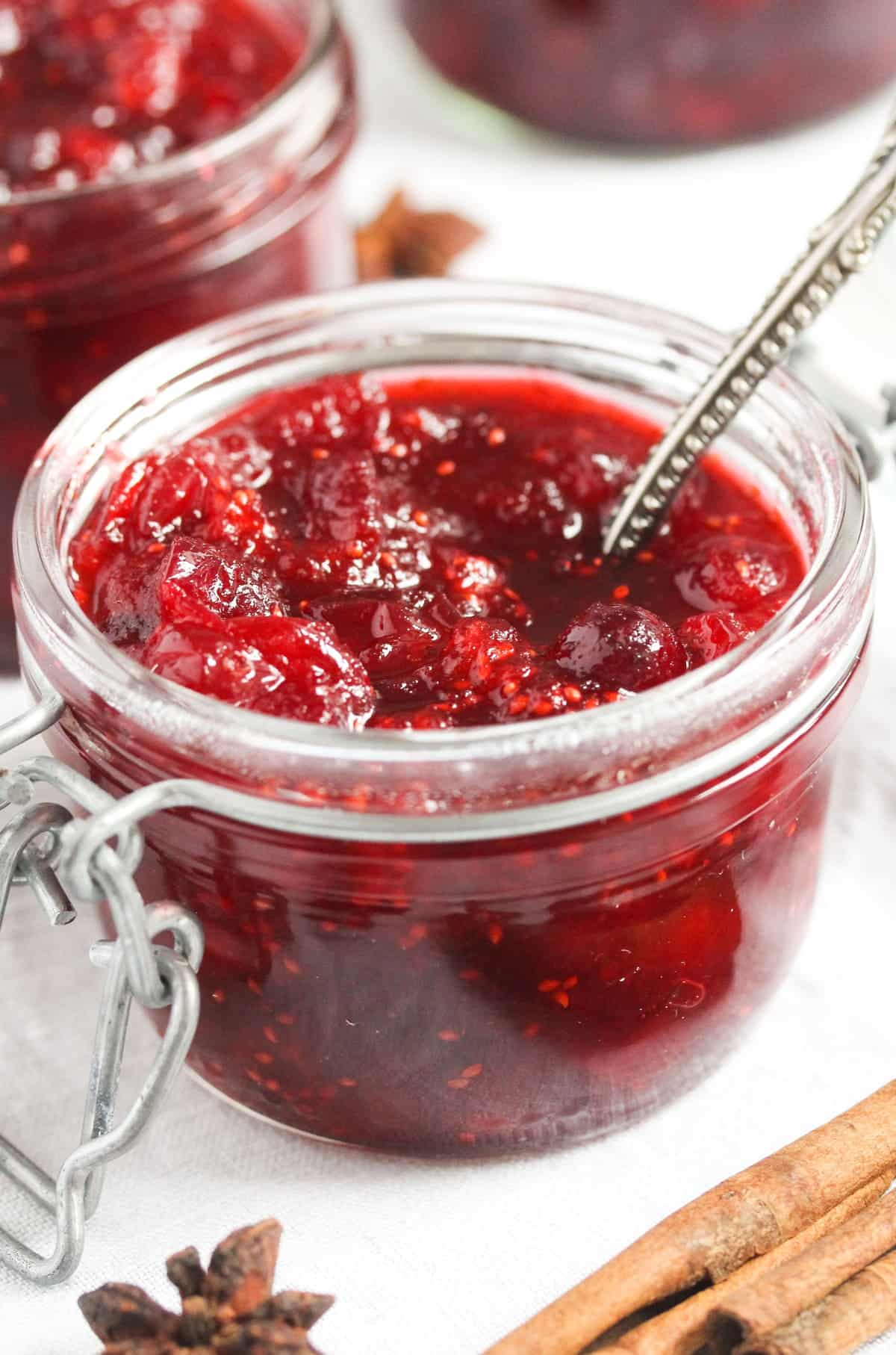 close up homemade cranberry sauce with a spoon in it and another jar behind.