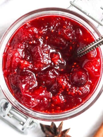 cranberry sauce for canning in a small jar with a spoon in it and spices around it.