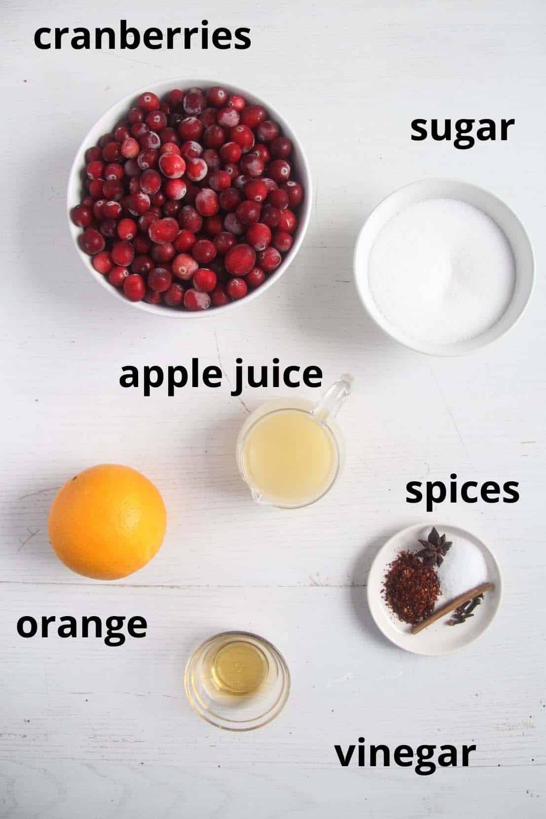cranberries, sugar, apple juice, orange, spices and vinegar in bowls on the table.