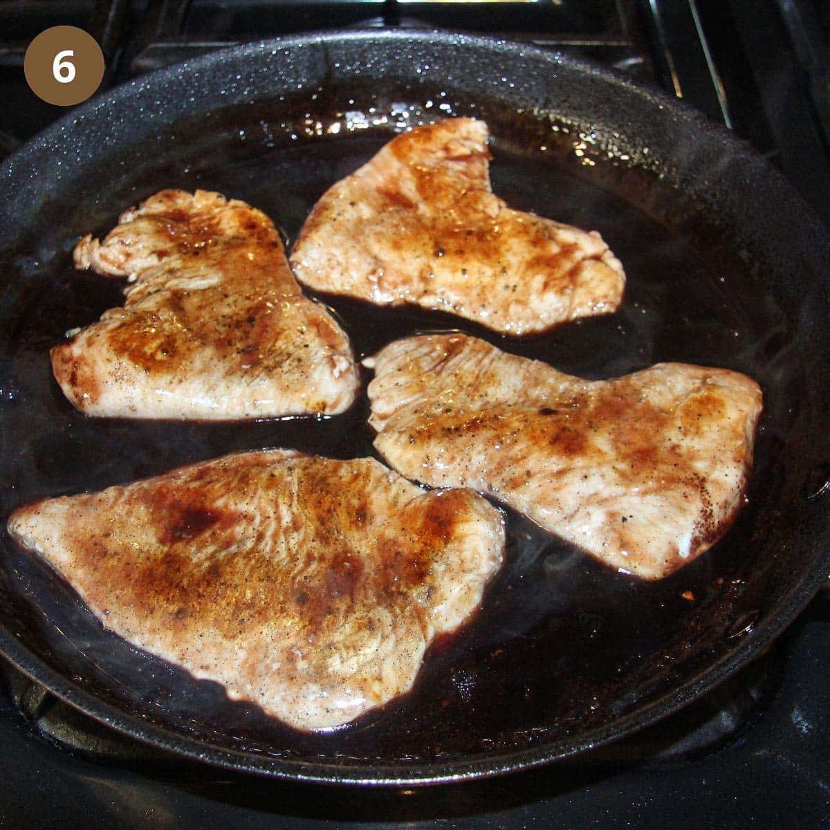 four turkey chops reheating in balsamic sauce in a pan.