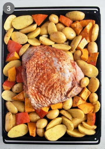 unbaked turkey thigh, potato and pumpkin pieces on a baking sheet.