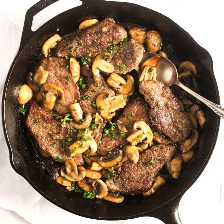 veal marsala served in a cast-iron pan with a spoon.