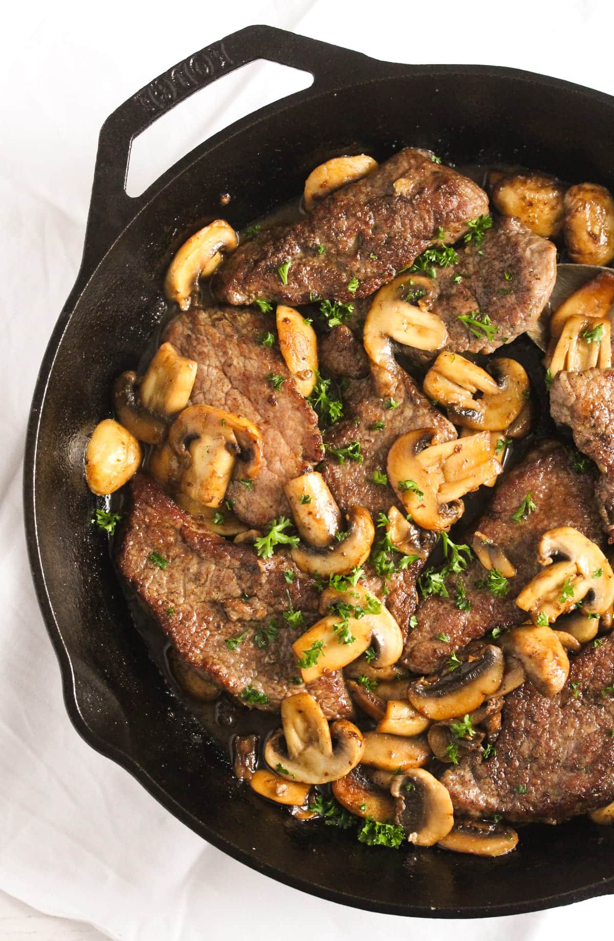 italian veal scallops with marsala sauce and mushrooms in a cast-iron pan.