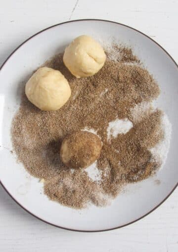 rolling dough balls in cinnamon sugar to make snickerdoodles.