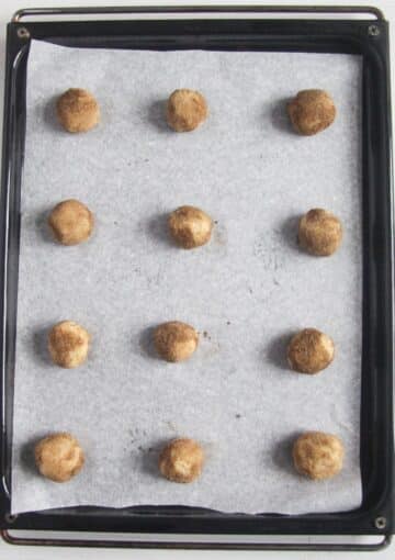 unbaked snickderdoodles on a baking sheet lined with white parchment paper.