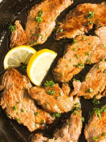 veal escalopes close up with lemon wedges.