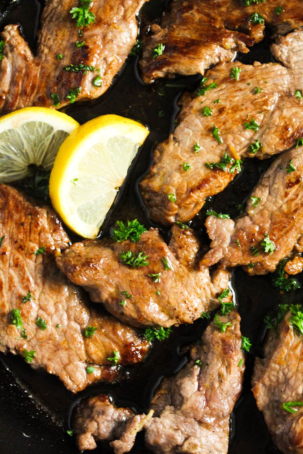 close up of many pieces of golden brown veal served with lemon wedges.
