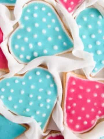 blue and pink heart cookies with white icing dots on a white cloth.
