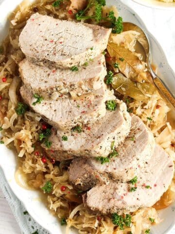 sliced pork roast on a bed of sauerkraut with a spoon on the side.