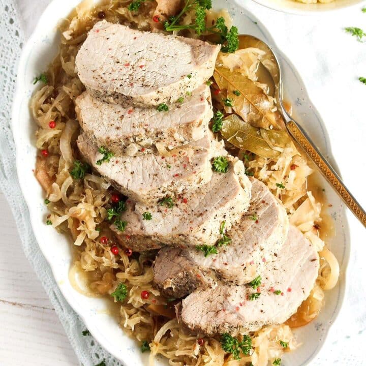 sliced pork roast on a bed of sauerkraut with a spoon on the side.