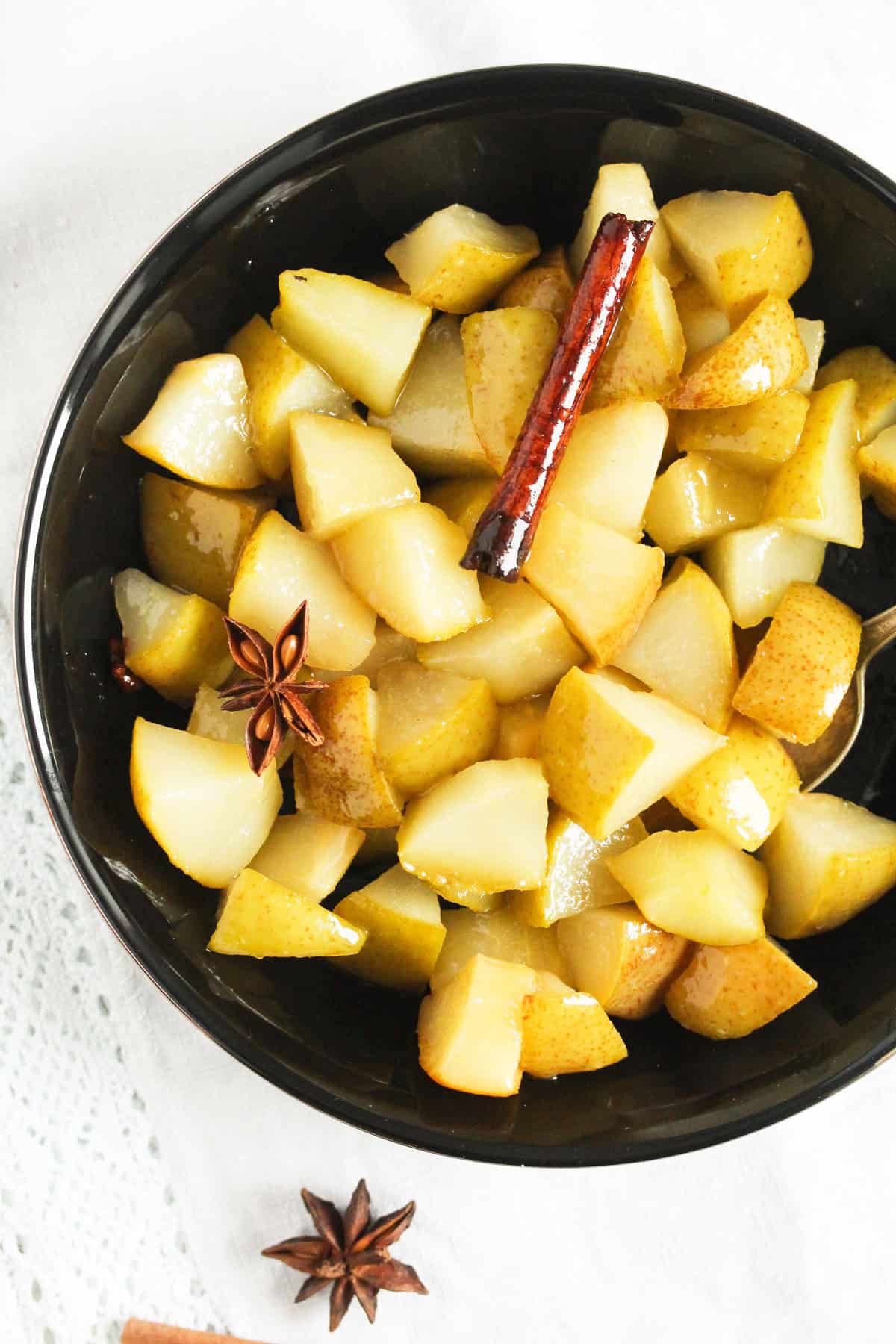 cubes pears poached with spices in a black bowl.