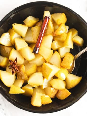 stewed pears with cinnamon and star anise in a black bowl.