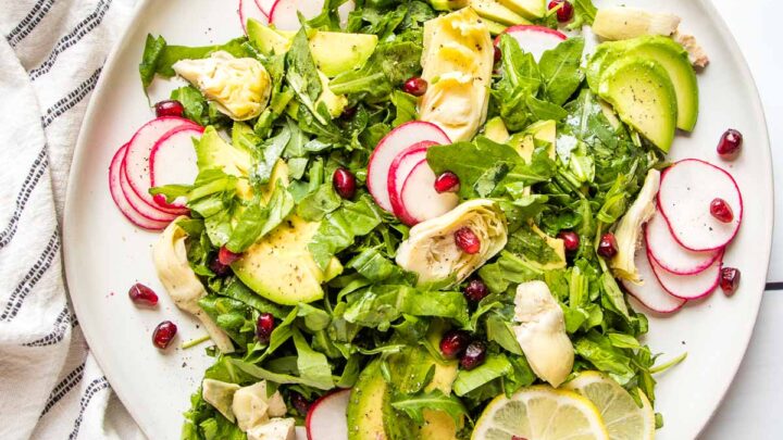 overhead view of a white plate with avocado salad with radishes and lemon.