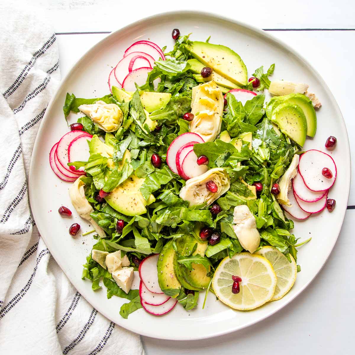 overhead view of a white plate with avocado salad with radishes and lemon.